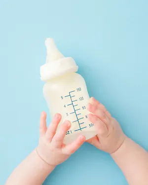 Baby holding a milk bottle with both hands on a light blue background.