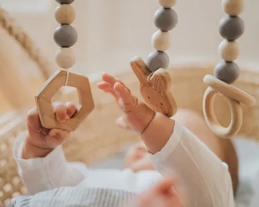 Baby reaching towards wooden hanging toys with geometric shapes in a crib.