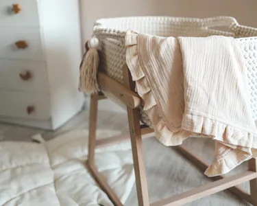 Empty baby bassinet with a light, soft blanket draped over the side, in a cozy nursery room.