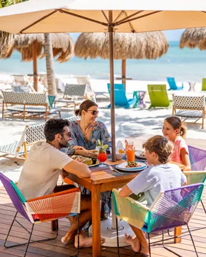 A family eating at a beachside restaurant under an umbrella.