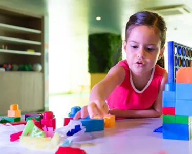 A girl concentrating on building a colorful structure with large plastic blocks while playing indoors.