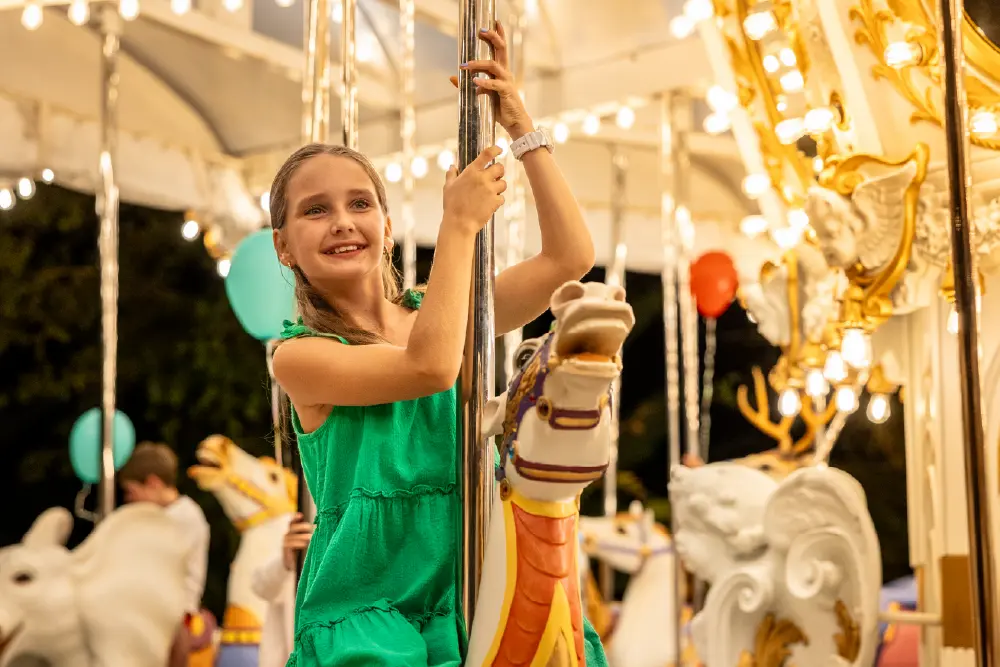 Smiling girl in green dress riding a carousel horse at night